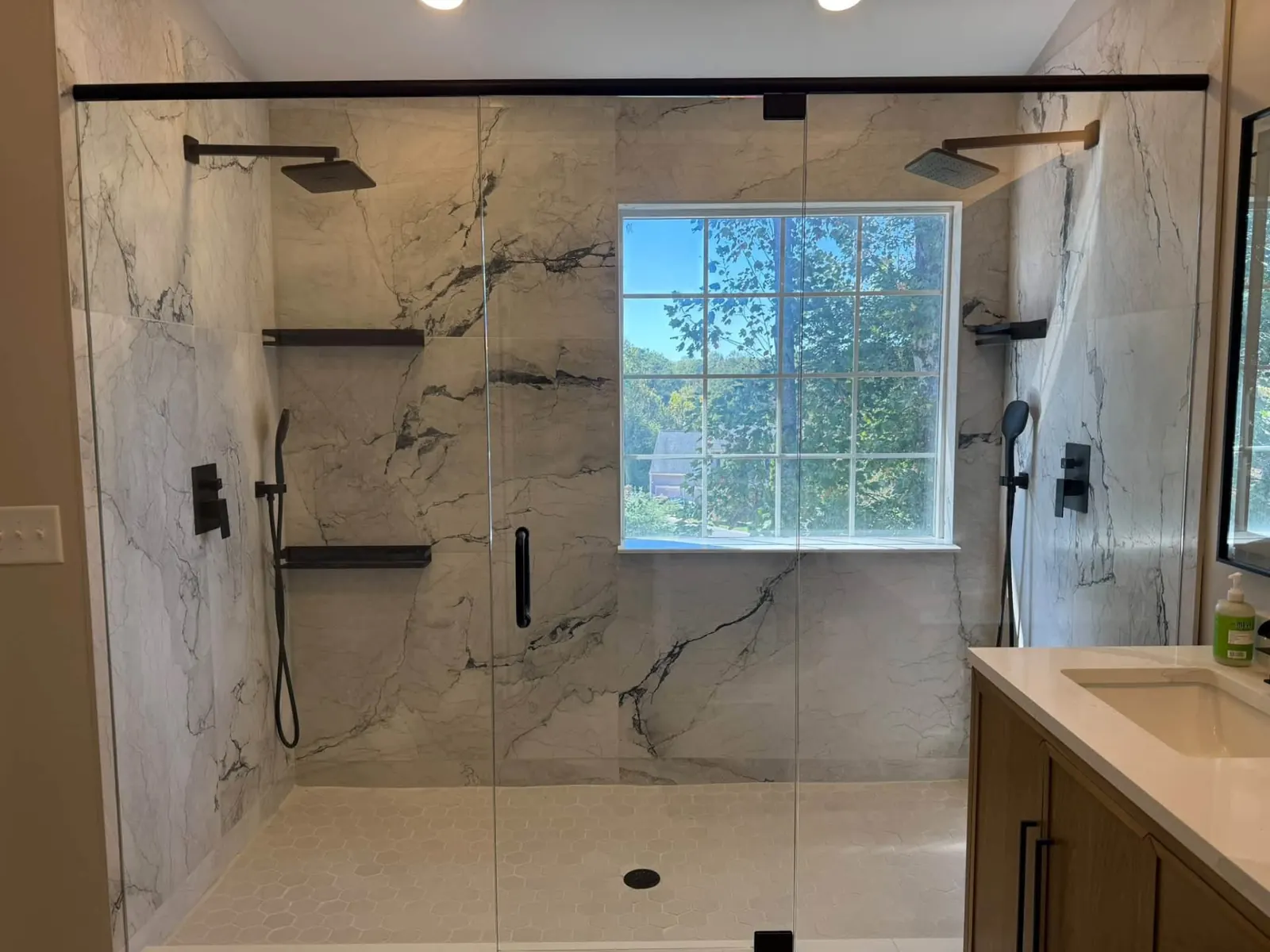Renown bathroom remodel: walk-in marble-look shower with dual rain heads, a center window and matte black fixtures