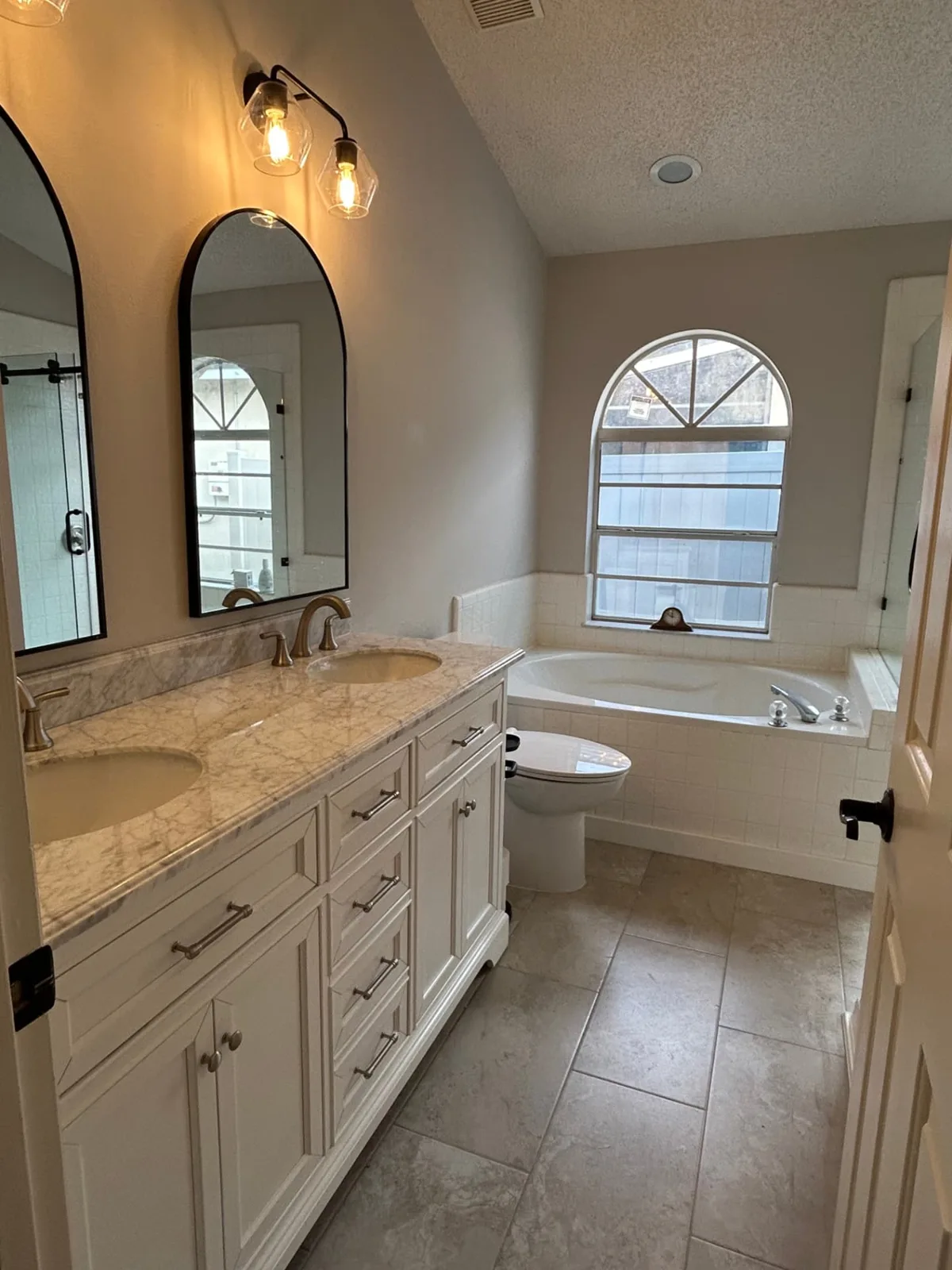 After: Primary bathroom with white double vanity, marble top and arched mirrors