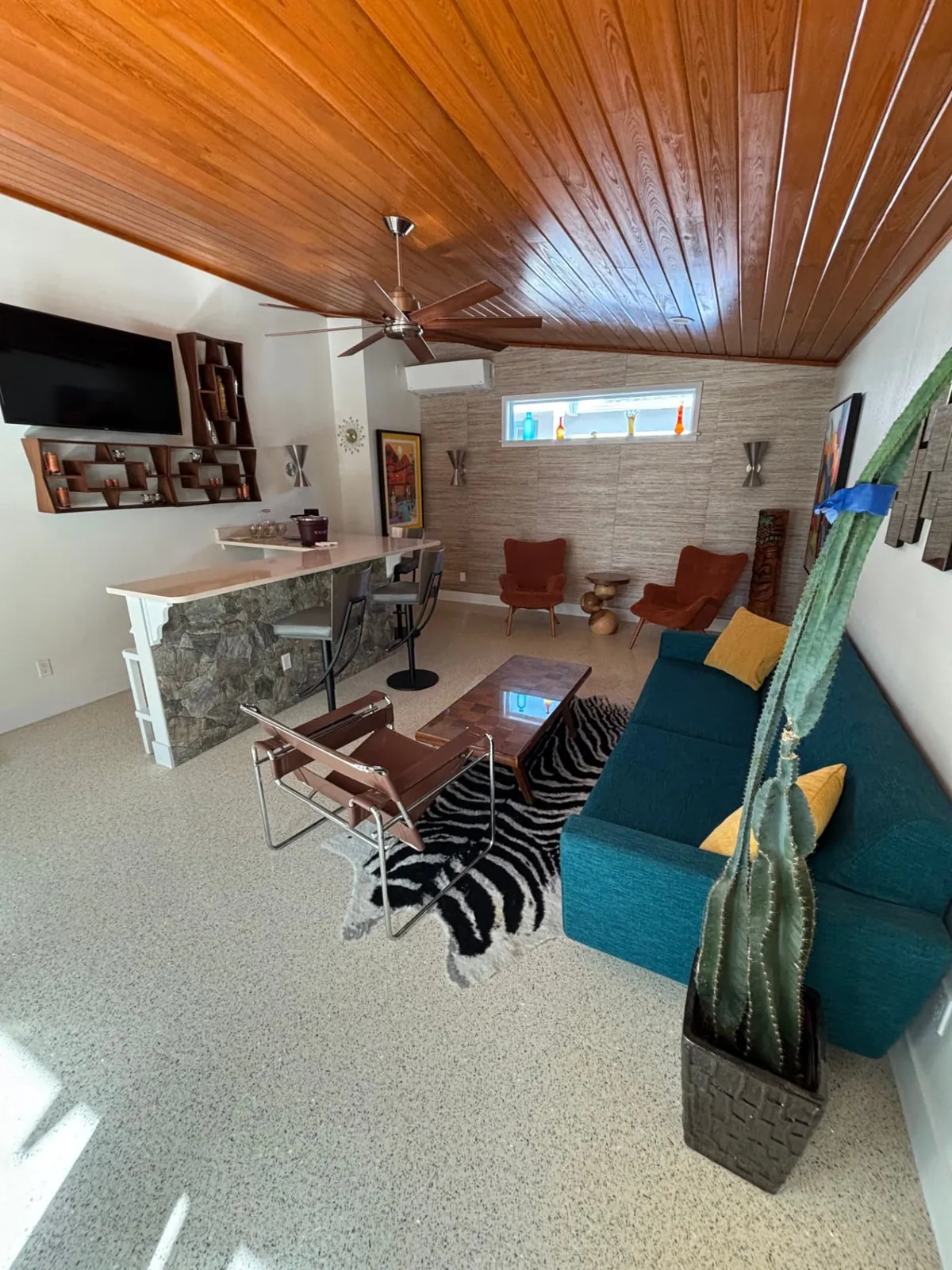 After: Lounge with a stained wood plank ceiling, stone-front bar and teal sofa