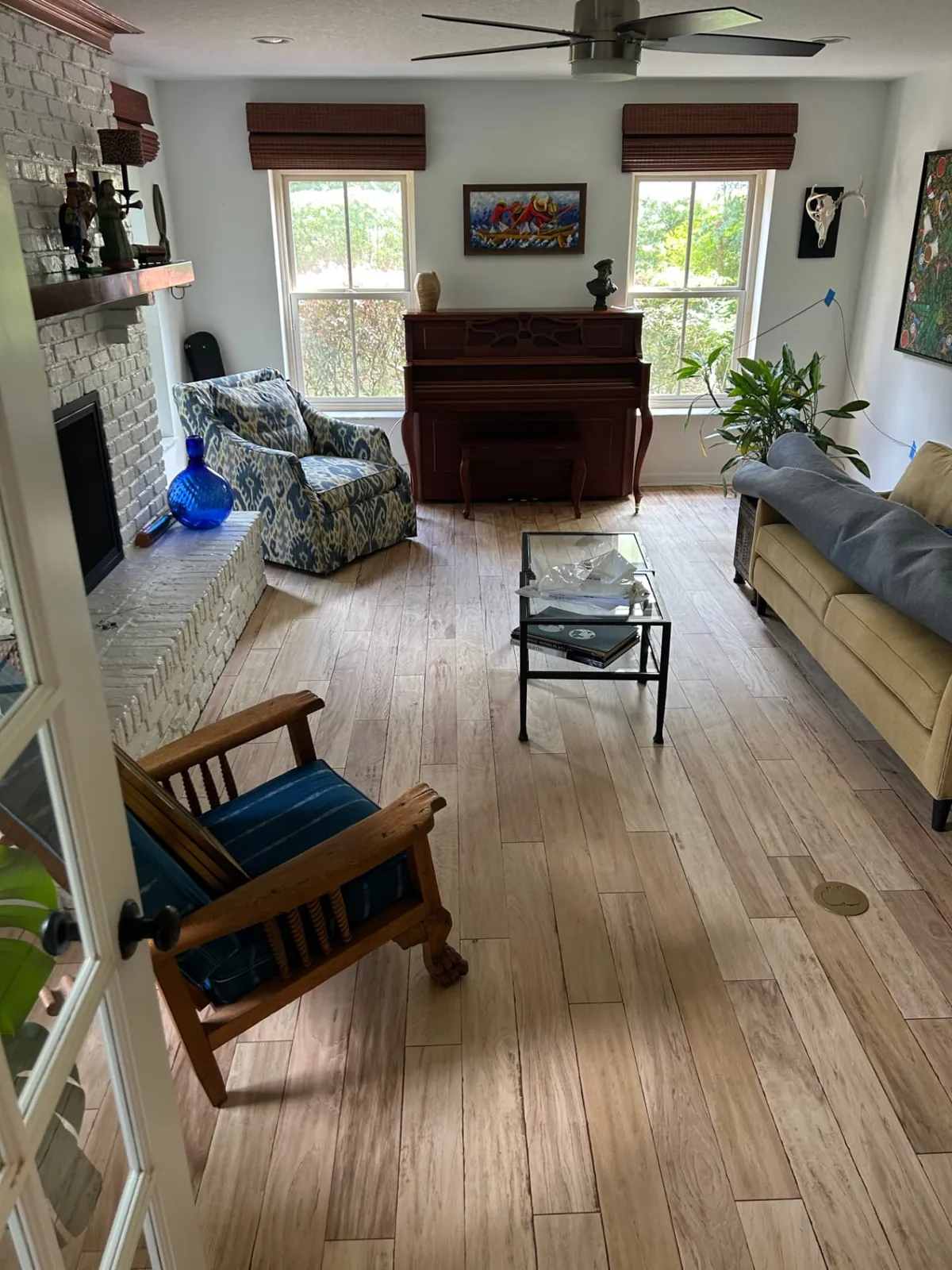 After: Family room with a white brick fireplace and refinished light, natural wood floors