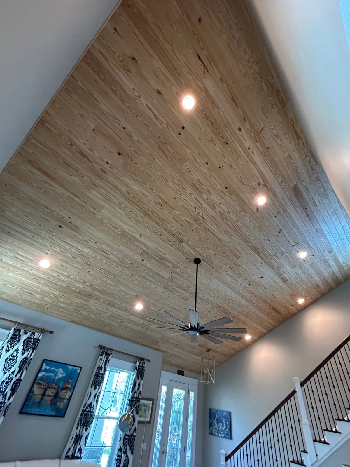 After: Vaulted great room ceiling covered in natural wood planks with recessed lights and ceiling fan