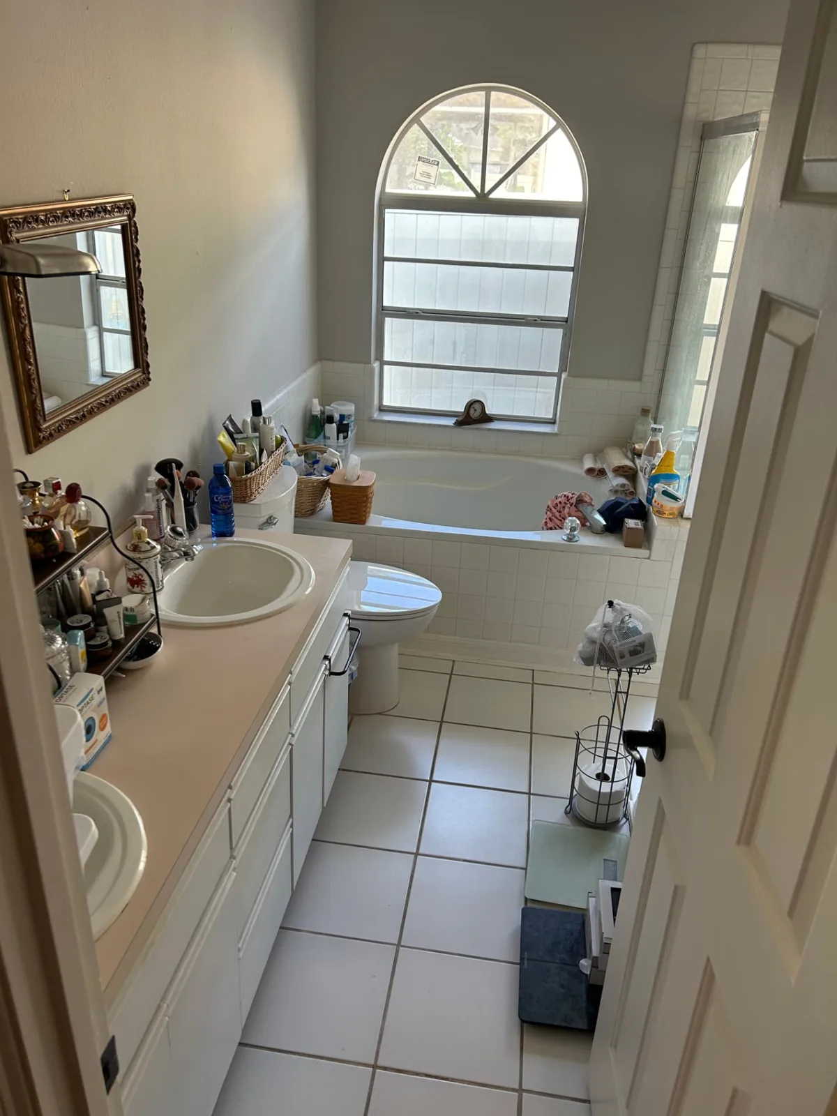 Before: Primary bathroom with white double vanity, marble top and arched mirrors