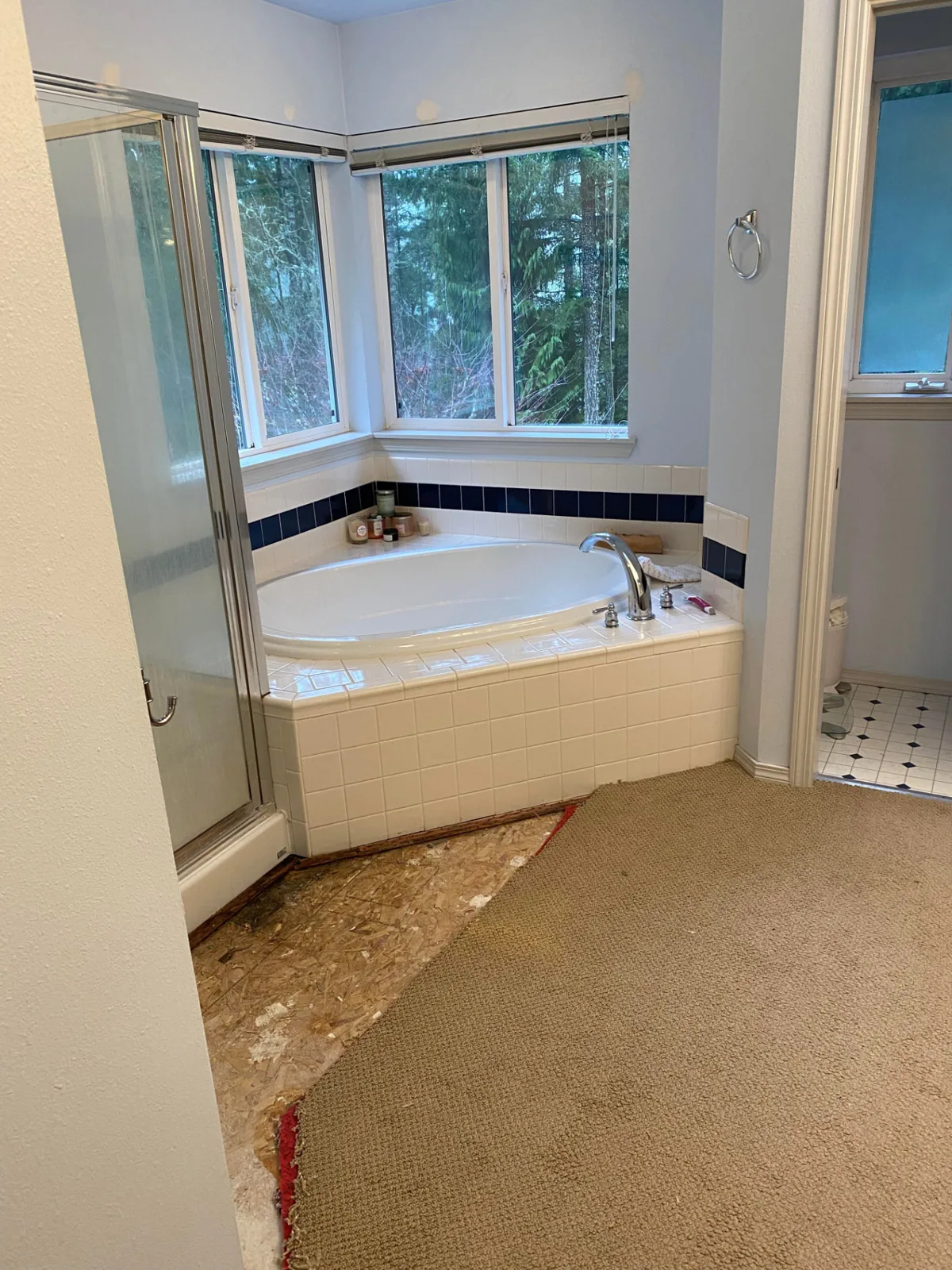 Before: Freestanding tub under corner windows in a marble-look porcelain bathroom