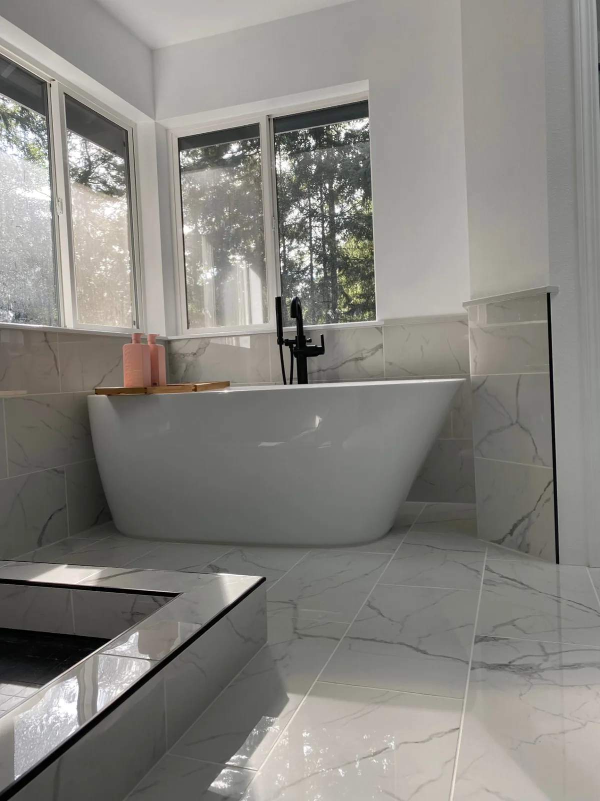 After: Freestanding tub under corner windows in a marble-look porcelain bathroom